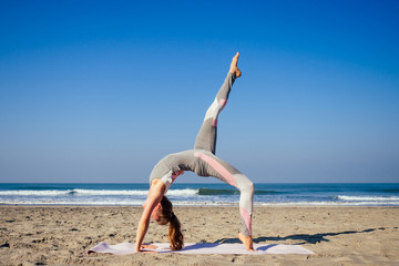 Fototapeta na wymiar Young healthy woman in a stylish one-piece jumpsuit practicing yoga on the beach at sunrise