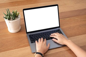 Fototapeta premium Mockup image of a woman using and typing on laptop with blank white desktop screen on wooden table in office
