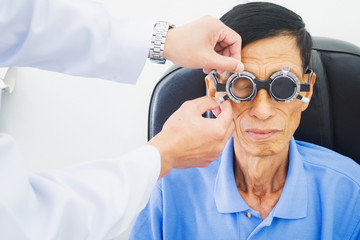 Elderly man having hes eyes examined by an eye doctor on a testing tool in modern clinic, optometry...