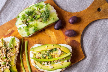 Sandwiches or tapas prepared with cream cheese , avocado and vegetables, on cutting board, over napkin background. Healthy food for lunch or breakfast. Flat lay.