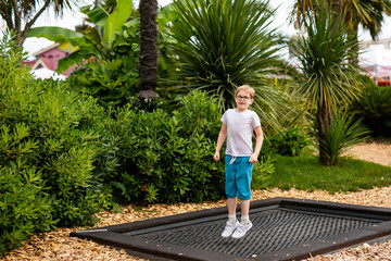 Fototapeta na wymiar Blonde boy with glasses 7 years old jumping in the children playground in the entertainment park