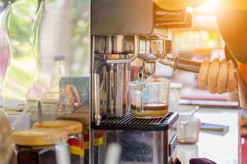 Women barista hand using coffee machine automatic preparing fresh coffee and pouring into glass cup