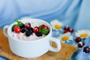 Jars of natural white yogurt with fruit salad with pink dragon fruit, berries and mint on wood table. Healthy eating. Copy space.blue background with white flowers
