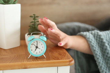 Sleepy woman turning off alarm clock in morning