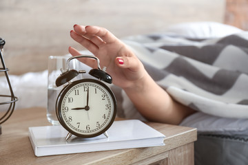 Sleepy woman turning off alarm clock in morning