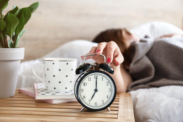 Sleepy woman turning off alarm clock in morning