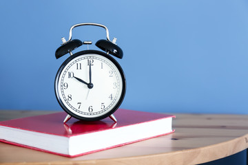 Alarm clock and book on table near color wall