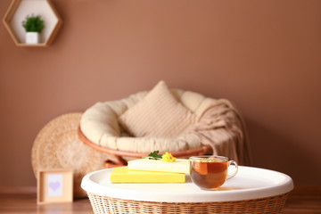 Cup of hot tea, flower and books on table in room