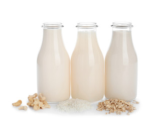 Bottles of different vegan milk on white background