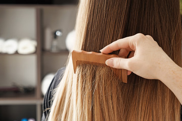 Hairdresser combing long hair of young woman in salon
