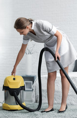Beautiful female housekeeper with vacuum cleaner in room