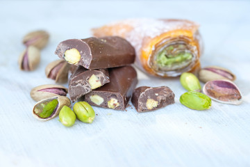 Eastern Turkish sweets with pistachios on a white wooden background. Chocolate candy with pistachios, baklava and pistachio nuts around.
