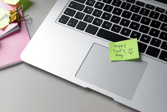 Laptop and sticky note with text HAPPY FOOL'S Day on grey background