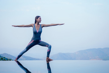 Fototapeta premium Beautiful woman practice yoga pose on the infinity pool above the mountain peak in the morning in front of beautiful nature views in india goa wildernest nature resorte .romance sunrise in mountains