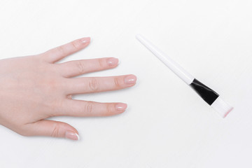 Woman hand is stretching to a makeup brush on the white wooden table background.