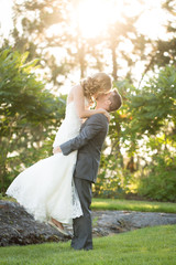 groom lifting and kissing beautiful bride on summer wedding day