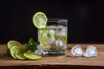 Summer cocktail mojito in glass, fruits and ice cubes on wooden background..