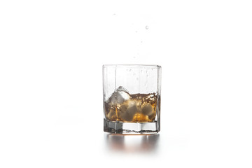 Whiskey splash from the fallen ice cube into glass with beverage on light background..