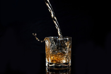 Whiskey pouring into glass with ice isolated on black background..