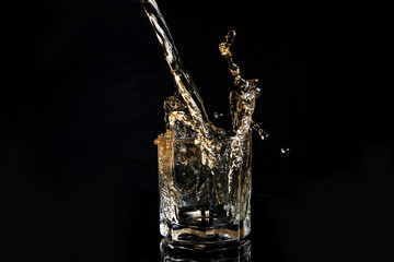 Whiskey pouring into glass with ice isolated on black background..