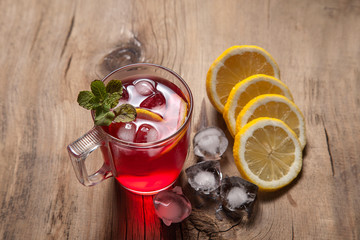 Hibiscus cold tea with ice, lemon and mint on vintage wooden background.