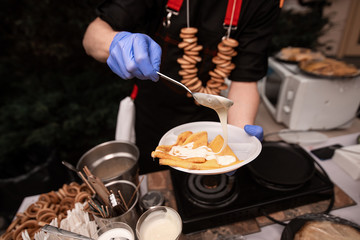 Hands cooks in blue gloves hold hold a plate of pancakes and impose a filling