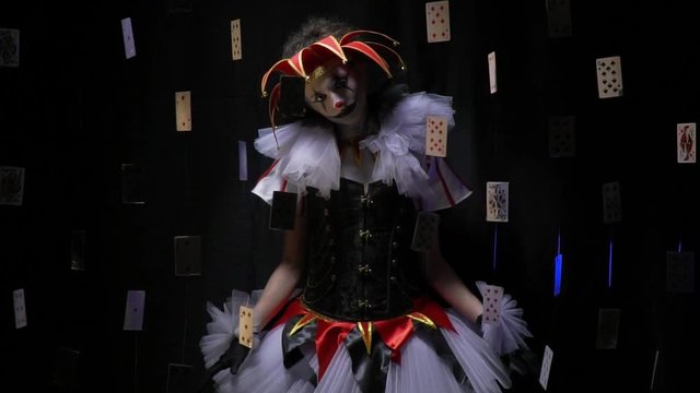 Beautiful female jester with makeup and a hat is shaking her head surrounded by floating playing cards