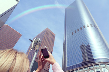 Woman tourist taking photo of skyscrapers by mobile smartphone in financial district in USA.