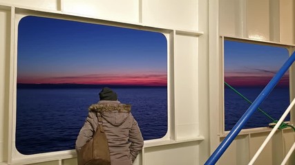 Lady looking through the scuttle while Irish ferry is leaving Cherbourgh in France to Dublin harbour during sunset - Ireland