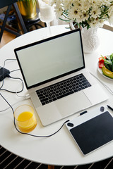 Opened laptop, graphics tablet and breakfast with juice on white table, empty screen for mockup design.