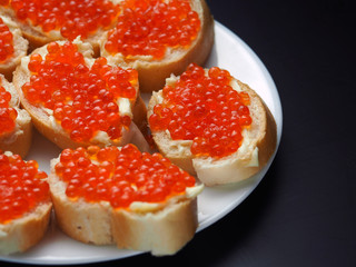 Red caviar on sandwiches in a plate on a dark background