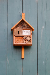 Insektenhotel in einem orange farbenen Haus an einer Holzwand