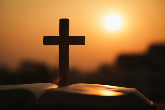 Silhouette of the wooden cross over opened bible with a bright sunrise as background , Christian, god. - Powered by Adobe