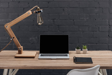 modern workplace with laptop with blank screen, plants, lamp and notebook on wooden table