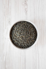 Dry green french lentils in gray bowl over white wooden background, top view. Flat lay, overhead, from above.