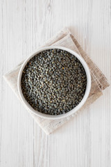 Overhead view, dry green french lentils in gray bowl over white wooden surface. Flat lay, top view, from above.