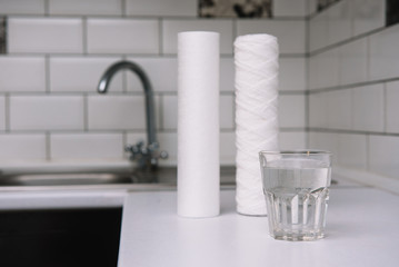 Water filters. Carbon cartridges and a glass on a white kitchen background. Household filtration system.