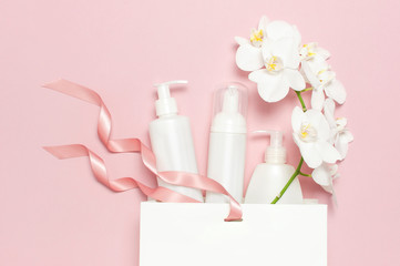 Obraz na płótnie Canvas Flat lay top view White cosmetic bottle containers gift bag White Phalaenopsis orchid flowers on pink background. Cosmetics SPA branding mock-up Natural organic beauty product concept Minimalism style