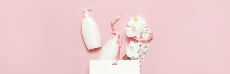 Flat lay top view White cosmetic bottle containers gift bag White Phalaenopsis orchid flowers on pink background. Cosmetics SPA branding mock-up Natural organic beauty product concept Minimalism style