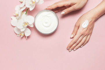 Young woman moisturizes her hand with cosmetic cream lotion opened container with cream body milk...