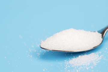 White sugar in spoon of turquoise blue background . copy space. soft focus
