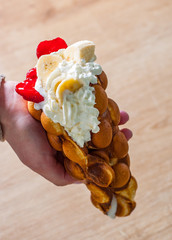 Hong Kong bubble waffles with ice cream, strawberry, banana in woman hand