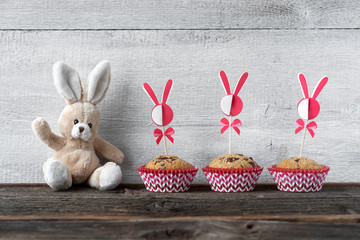 Osterhase sitzt mit Muffins vor einer Holzwand