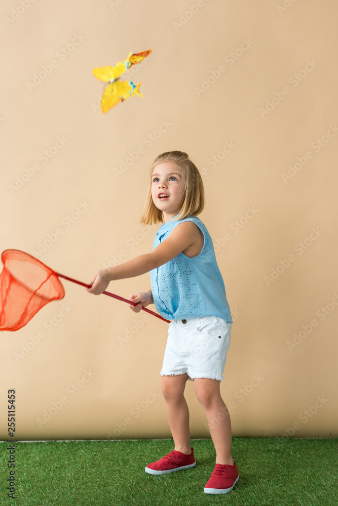 Wall mural cute kid catching butterfly with red butterfly net on beige background