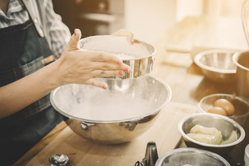 Obraz na płótnie Canvas women are sifting flour to make bakery; happy family in kitchen