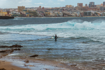 Tourism and travel. Windy day on the ocean. Surfer with a board. Canary Islands, Gran Canaria, Atlantic Ocean. Tropics. City of Las Palmas