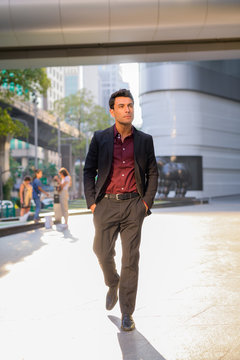 Young Handsome Hispanic Businessman Thinking And Walking Outside The Office Building