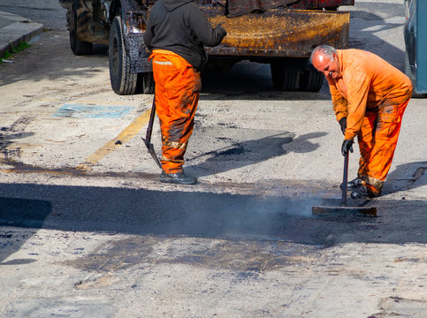 Worker regulate laying new asphalt to patch a bump in the road.