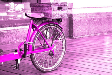 Fototapeta na wymiar View of a bright pink bike with a basket standing on the wooden floor outside.