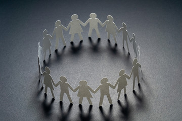 Circle of paper people holding hands on dark surface. Community, brotherhood concept. Society and support.